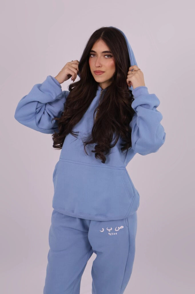 Woman wearing a blue tracksuit with text on the pants against a light gray background